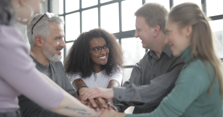 Team joining hands in a circle, smiling and supporting each other.