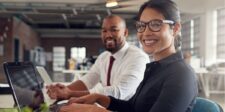 Smiling professionals working at laptops in an office.