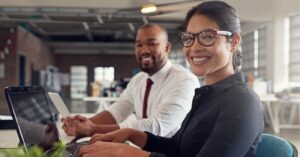 Smiling professionals working at laptops in an office.