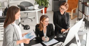 Three colleagues discussing charts and data in an office setting.