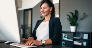 Professional woman smiling while working at a computer in an office.