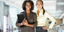 What Does It Mean to Be a Professional Today? Two women smiling in an office setting. One holds a folder.