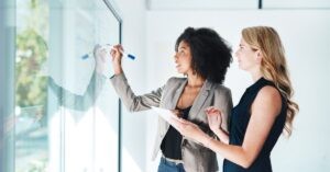 Two professionals brainstorming at a whiteboard in an office setting.