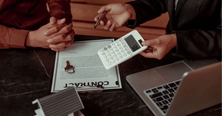 Hands negotiating over a contract with a calculator and laptop.