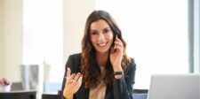 Person smiling while talking on the phone, sitting at a desk.