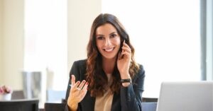 Person smiling while talking on the phone, sitting at a desk.