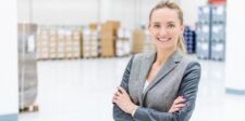 Smiling professional woman standing confidently in a warehouse setting.