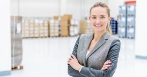 Smiling professional woman standing confidently in a warehouse setting.