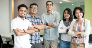 Group of five people standing in an office with arms crossed, smiling.