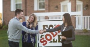 Couple shaking hands with a real estate agent in front of a "Sold" sign.