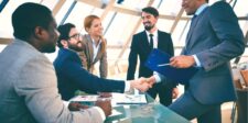 Business professionals in a meeting, shaking hands with smiles.