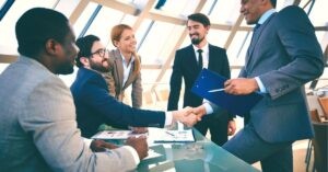 Business professionals in a meeting, shaking hands with smiles.