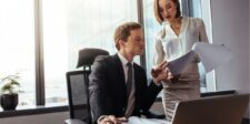 Man sitting at a desk reviewing documents with a woman in an office.