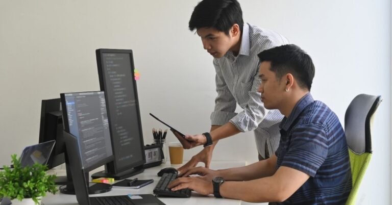 Two developers collaborating on a coding project at a desk.