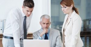 Three business professionals focused on a laptop screen during a meeting.