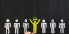 Product Positioning: Stand Out in a Crowded Market Chalk drawing of white figures on a blackboard, with a yellow figure and lightbulb, symbolizing a unique idea.