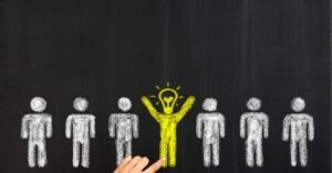 Chalk drawing of white figures on a blackboard, with a yellow figure and lightbulb, symbolizing a unique idea.