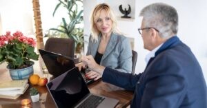 Two professionals having a discussion at a table with laptops and flowers.
