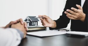 Discussion over a model house and contract on a desk.