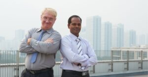 Two professionals standing confidently on a rooftop with a cityscape in the background.