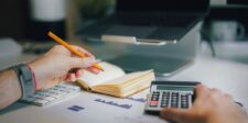 Person calculating finances with a notebook, keyboard, calculator, and financial charts on a desk—demonstrating money planning as a way to manage money stress.