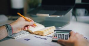 Person calculating finances with a notebook, keyboard, calculator, and financial charts on a desk—demonstrating money planning as a way to manage money stress.