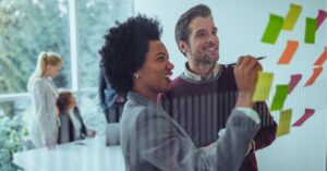 Colleagues brainstorming with colorful sticky notes on a glass wall in a bright office.