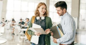 Two colleagues in a casual discussion holding tablets and notebooks.
