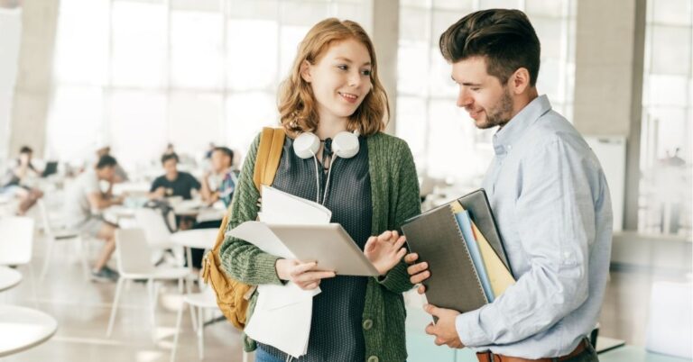 Two colleagues in a casual discussion holding tablets and notebooks.