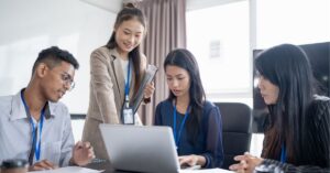 A diverse team collaborating and discussing ideas around a laptop in a meeting room.