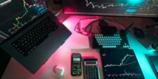 How to Set Up and Optimize Your Trading Platform Multi-device trading setup featuring a laptop, smartphone, tablet, calculator, and monitor displaying candlestick charts and trading data in a neon-lit workspace.
