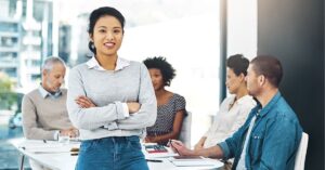 Confident professional standing in front of colleagues during a meeting.