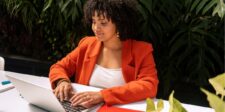 Zero Click Content Guide with Powerful Tips That Work Woman in an orange blazer working on a laptop at an outdoor table.