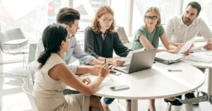 Team collaborating around a table with laptops and documents.