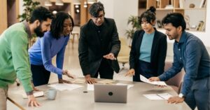 Team collaborating around a table with a laptop and documents.
