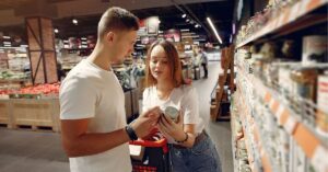 Couple shopping in a grocery store aisle, examining a canned product.