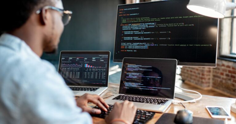 Developer working at a desk with multiple screens displaying code and analytics dashboards, illustrating enterprise web development.