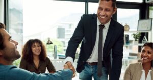Business professionals shaking hands in a meeting room, smiling.