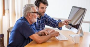 Two men working together on a computer, one pointing at the screen.