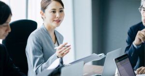 Businesswoman presenting in a meeting with colleagues using laptops.