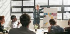 Person giving a presentation with sticky notes on a board in a meeting room.