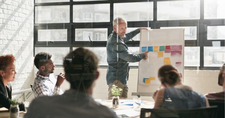 Person giving a presentation with sticky notes on a board in a meeting room.