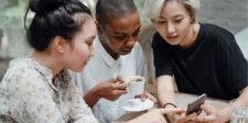Three friends sharing a moment over coffee and a smartphone.
