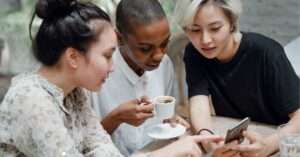 Three friends sharing a moment over coffee and a smartphone.