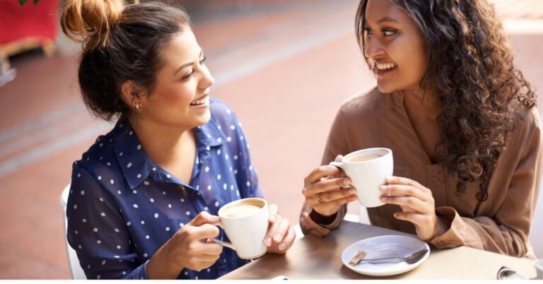 Two women smiling and chatting over coffee at a cafe table.