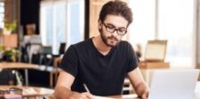 Why You Need Press Release Writers: What You Need to Know Man in glasses writing at a desk with a laptop.
