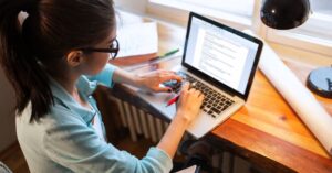 Person writing a blog post on a laptop at a desk.