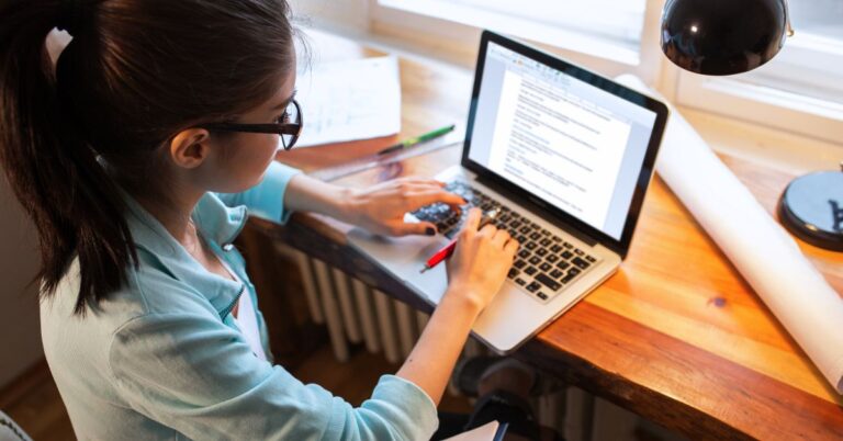 Person writing a blog post on a laptop at a desk.