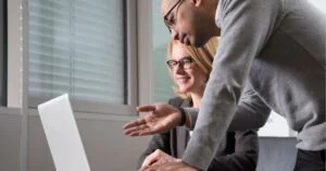 Two colleagues collaborating at a laptop in an office setting.