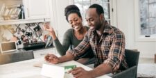 Couple smiling while working on a tablet at home.